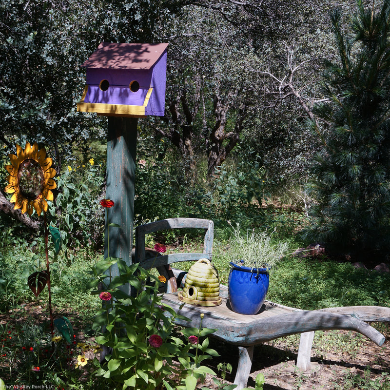 An old wooden wheelbarrow and a colorful bird house sit near the greenhouse.